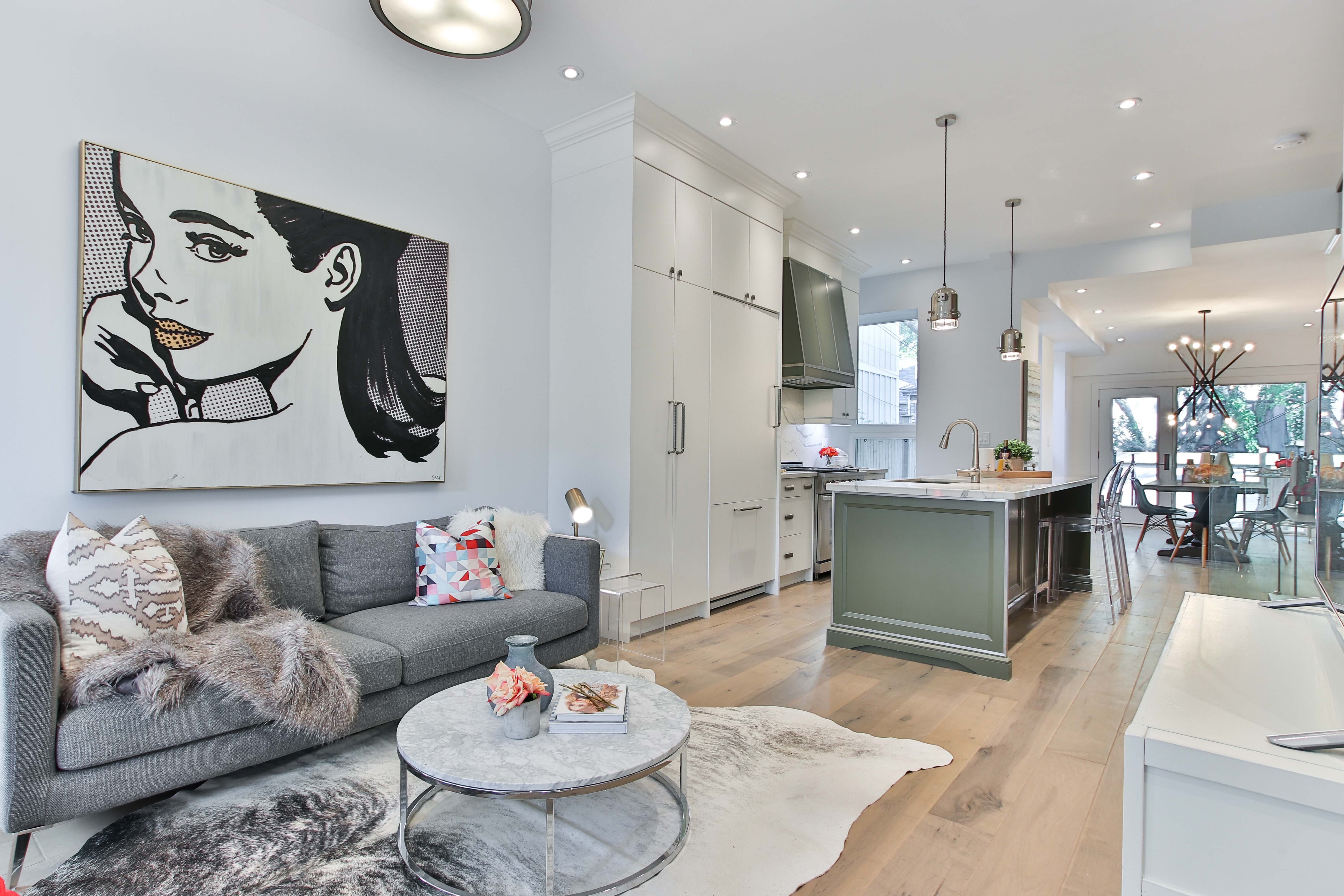 Modern living room with a large black-and-white pop-art portrait, grey sofa, marble coffee table, and open kitchen