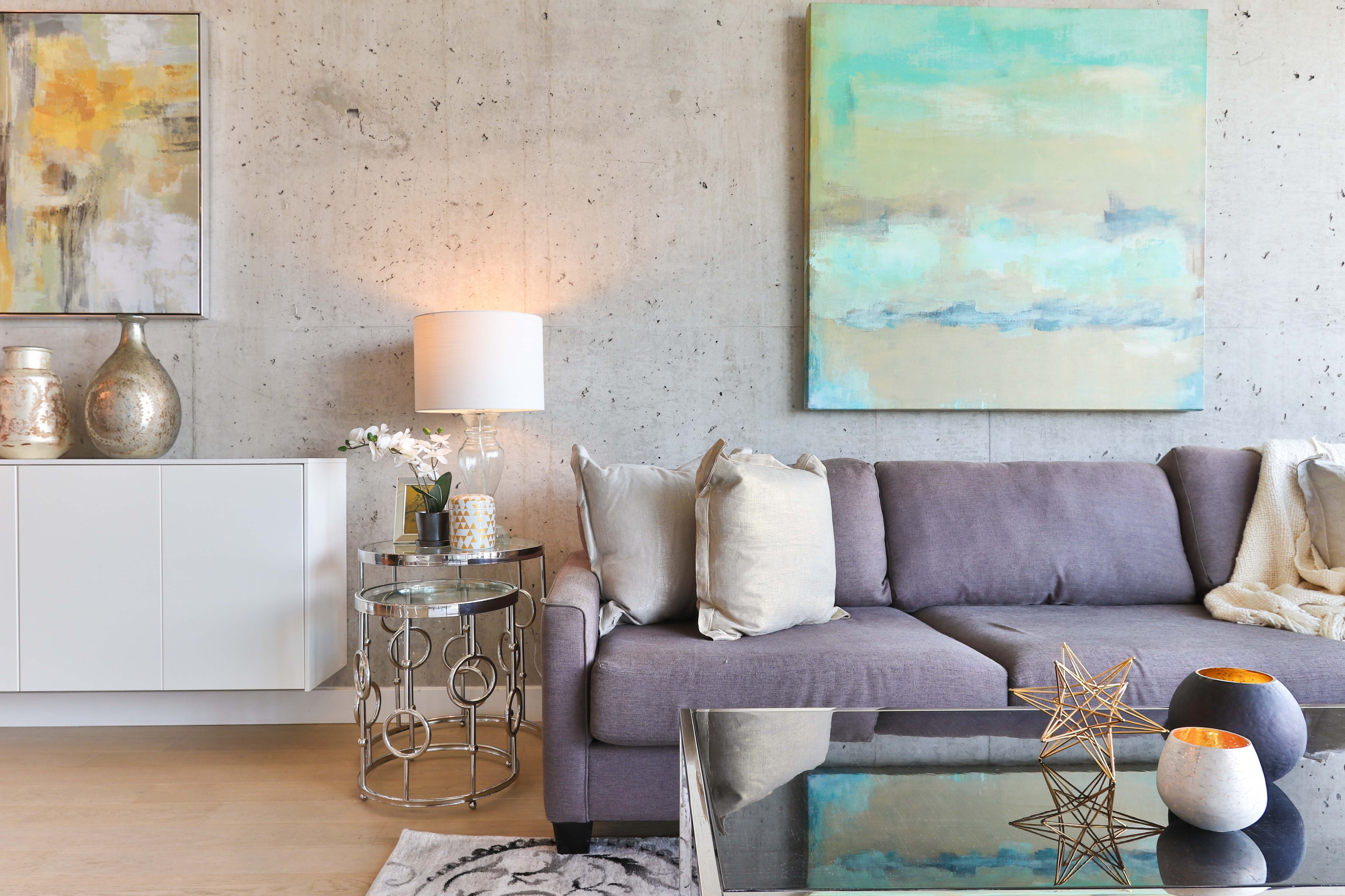 Modern living room with a grey sofa, concrete accent wall, and abstract art